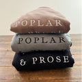 Stack of folded clothing with 'POPLAR & PROSE' branding on a wooden surface.
